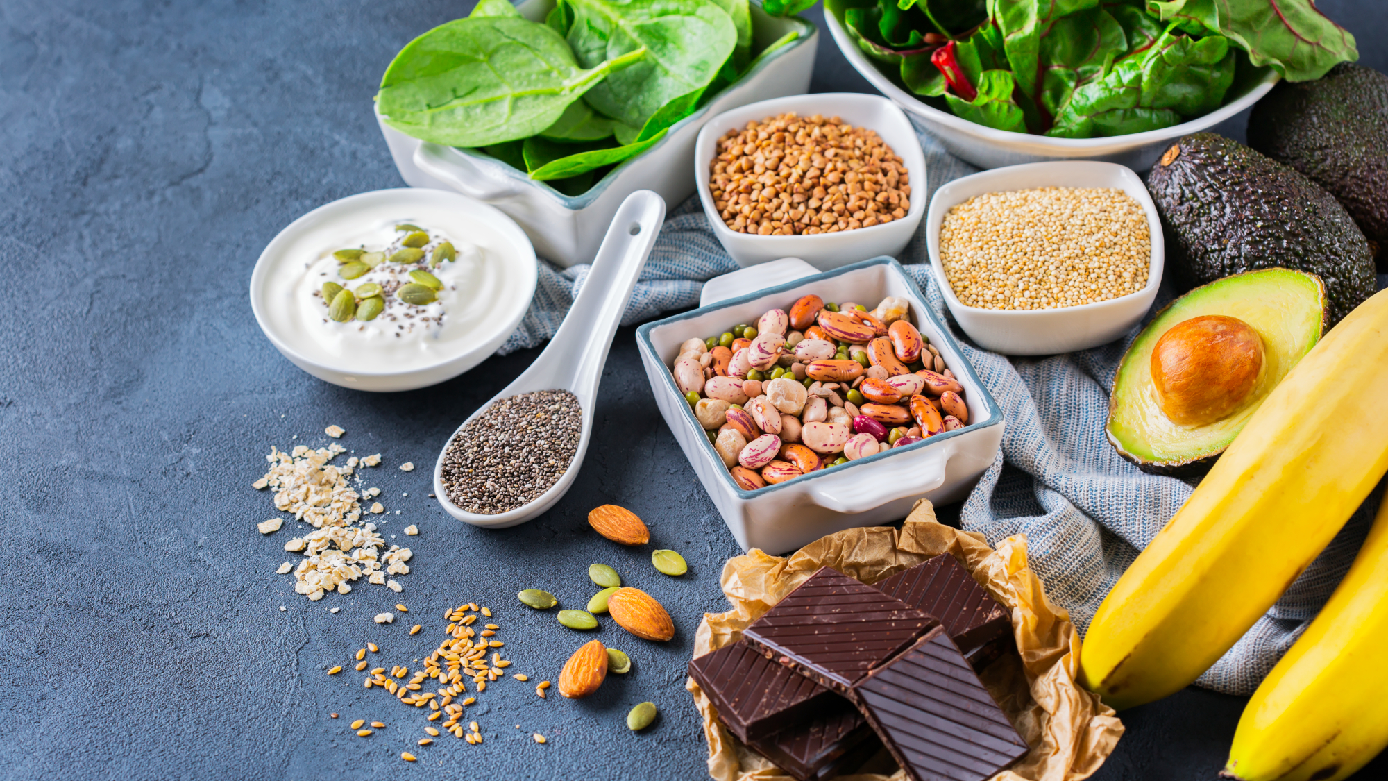 Assortment of healthy high magnesium sources food Healthy food nutrition dieting concept. Assortment of high magnesium sources. Banana chocolate spinach chard, avocado, buckwheat, sesame chia flax seeds, yogurt, nuts, beans oat