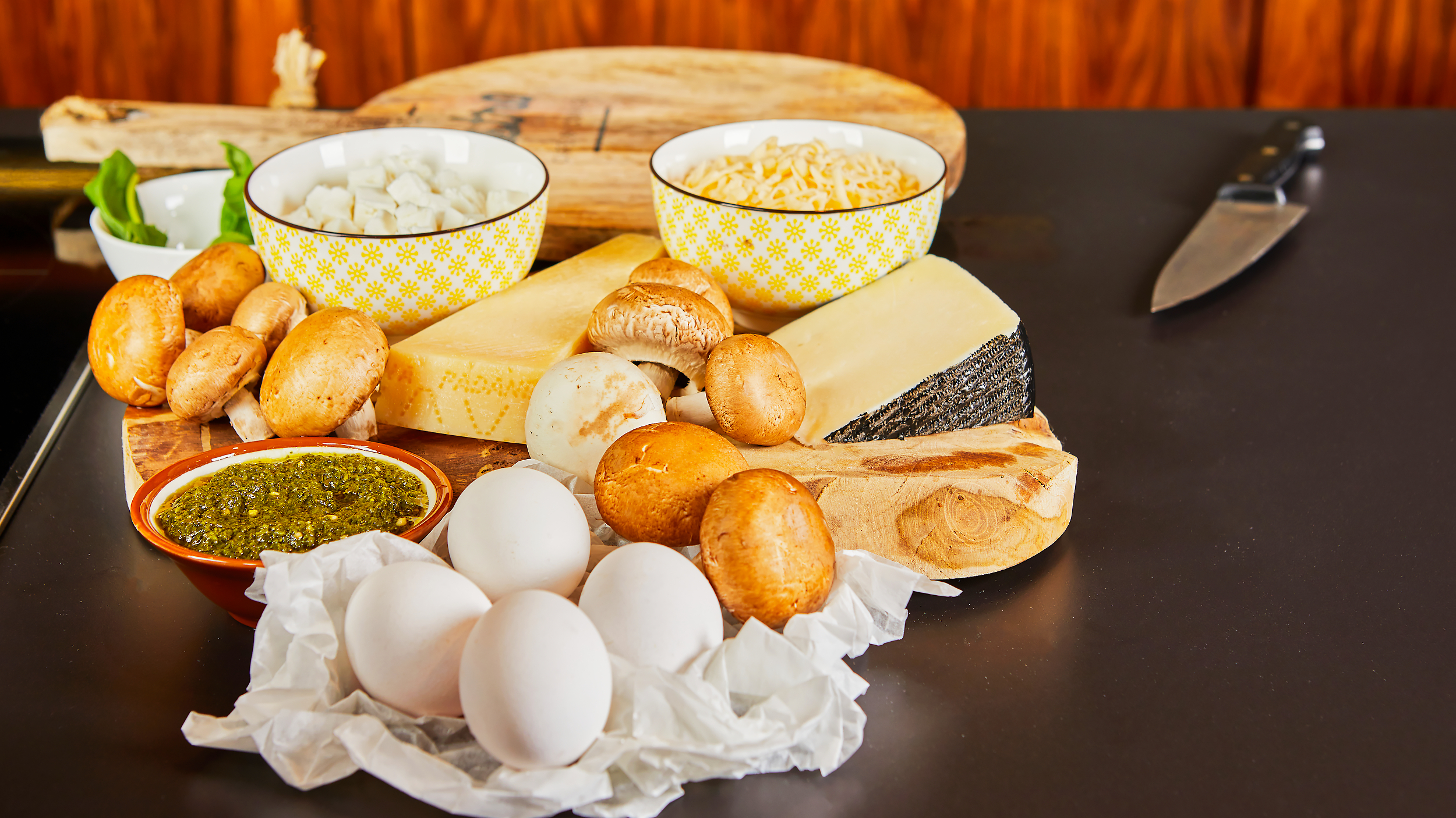 A selection of fresh eggs, cheeses, mushrooms, and herbs laid out on a kitchen counter, perfect for preparing a delicious homemade meal Eggs and cheese